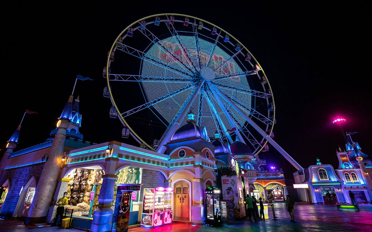 Ferris wheel illuminated at night with visitors at Global Village Dubai entrance.
