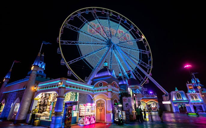 Ferris wheel illuminated at night with visitors at Global Village Dubai entrance.