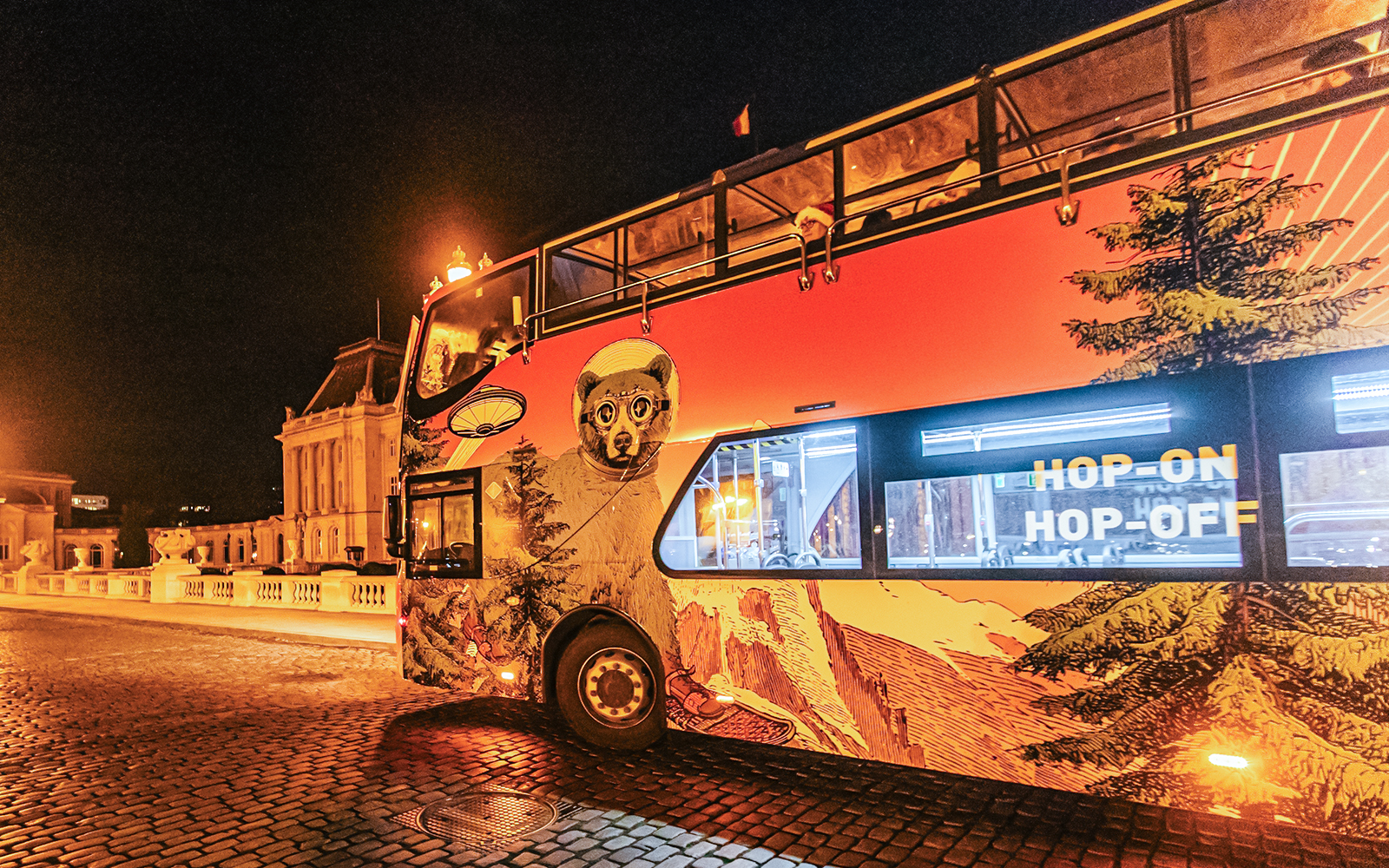 Brussels hop-on hop-off bus at night with festive lights and city architecture.