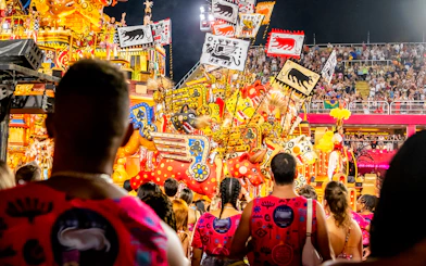 Spectators watching vibrant floats and performers at Rio Carnival 2027, Marquês de Sapucaí, Rio de Janeiro.