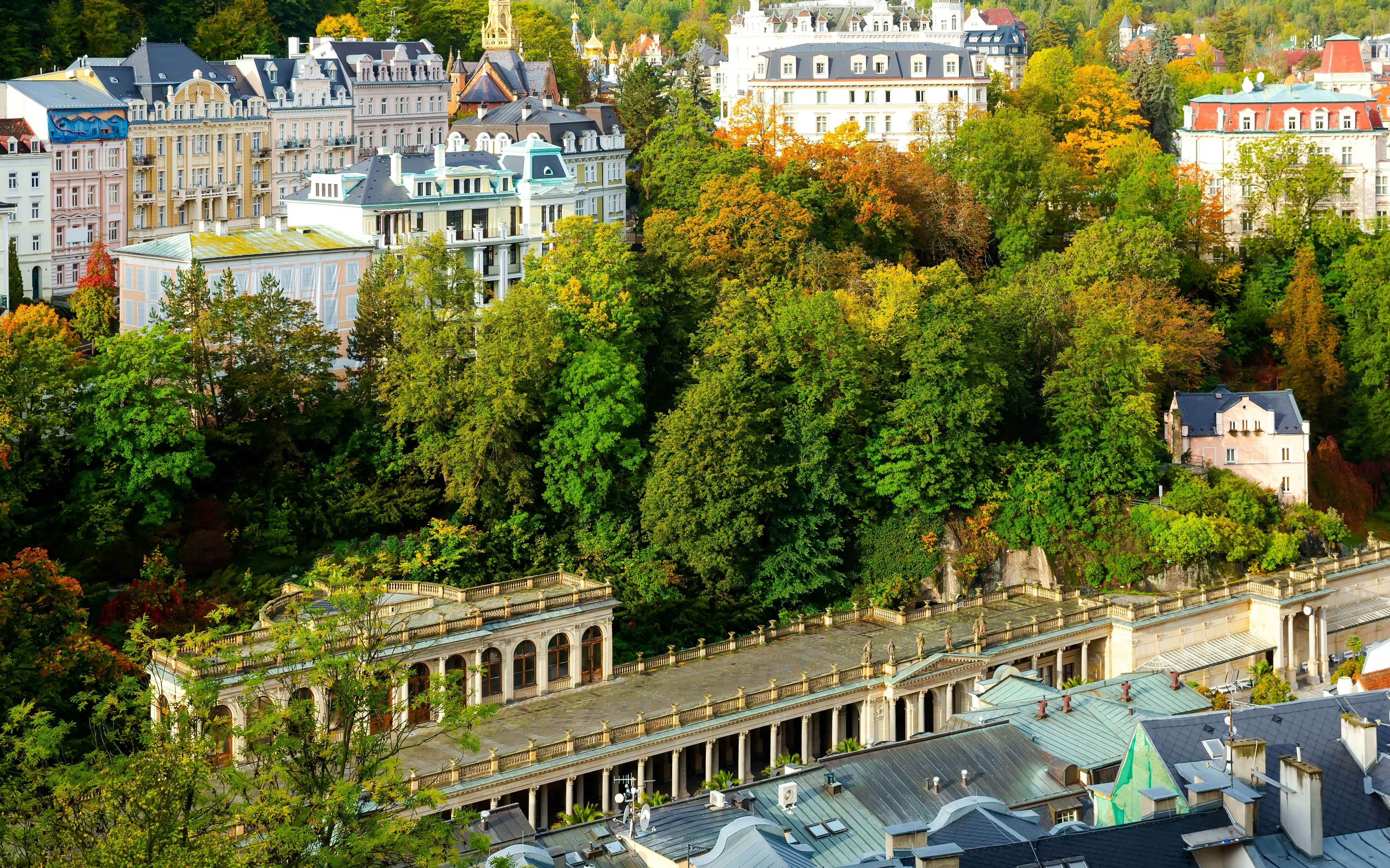 Colorful cityscape of Karlovy Vary with Mill Colonnade surrounded by lush greenery.