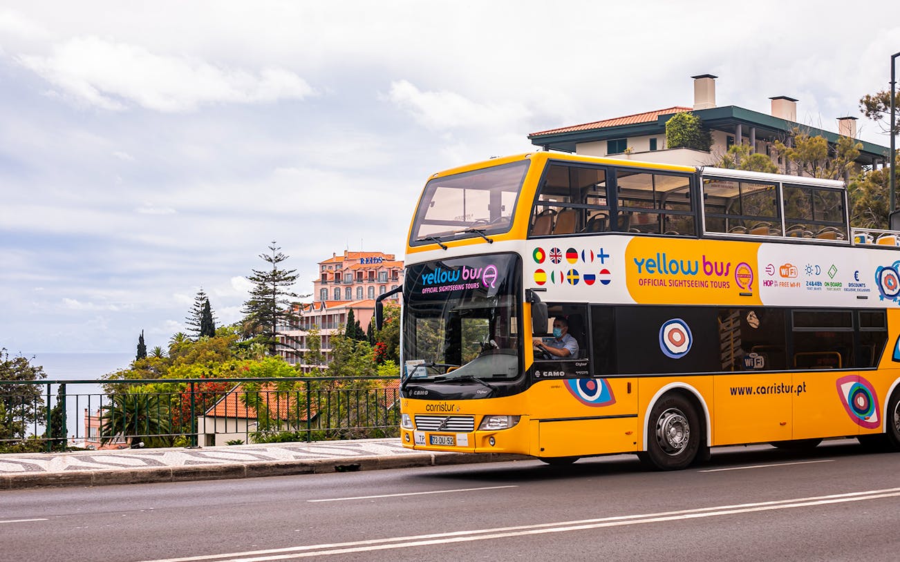 Yellow sightseeing bus in Funchal, Madeira, with scenic view of buildings and trees.
