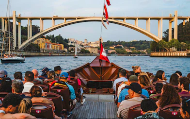 Tourists on a boat ride with view of Arrábida Bridge and Douro River in Porto, Portugal.