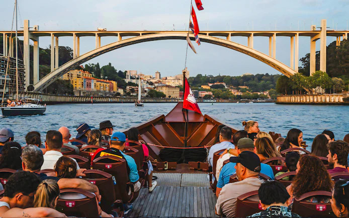 Tourists on a boat ride with view of Arrábida Bridge and Douro River in Porto, Portugal.