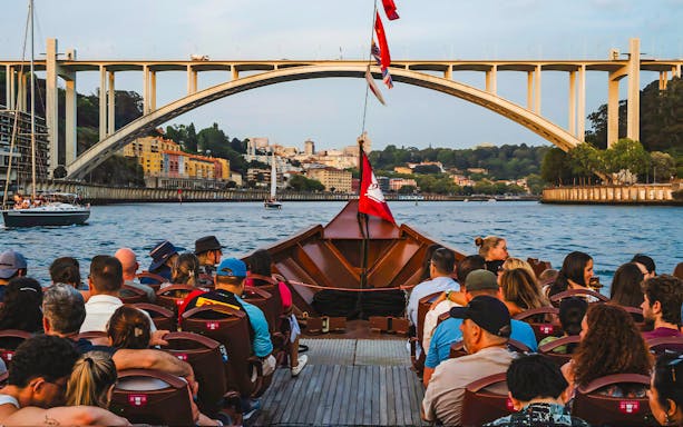Tourists on a boat ride with view of Arrábida Bridge and Douro River in Porto, Portugal.