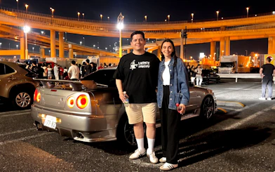 Guests at JDM Tokyo car meetup night tour with skyline and cars in background.