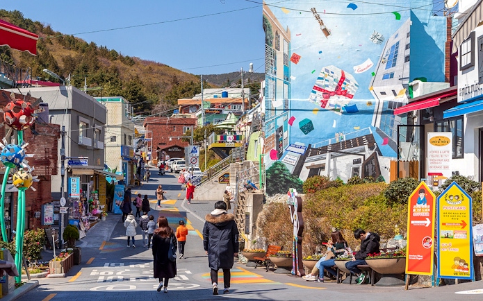 Street view of Gamcheon Culture Village in Busan with colorful murals and tourists exploring.