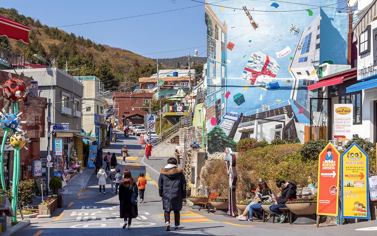 Street view of Gamcheon Culture Village in Busan with colorful murals and tourists exploring.