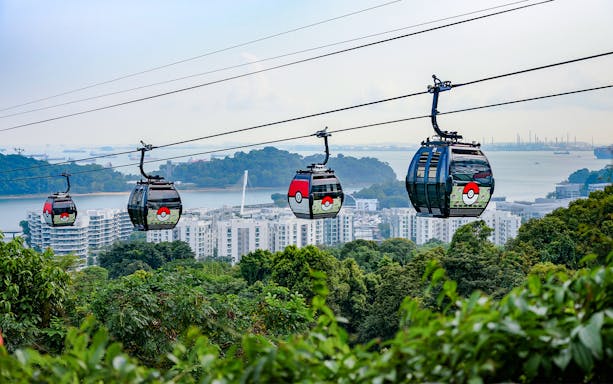 Cable cars with themed designs traveling over Sentosa, Singapore, with cityscape and water views.