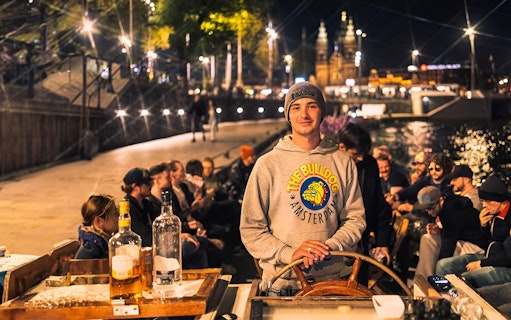 Amsterdam canal cruise with people enjoying drinks and a smoke-friendly atmosphere at night.