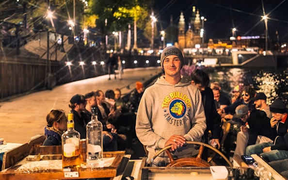 Amsterdam canal cruise with people enjoying drinks and a smoke-friendly atmosphere at night.