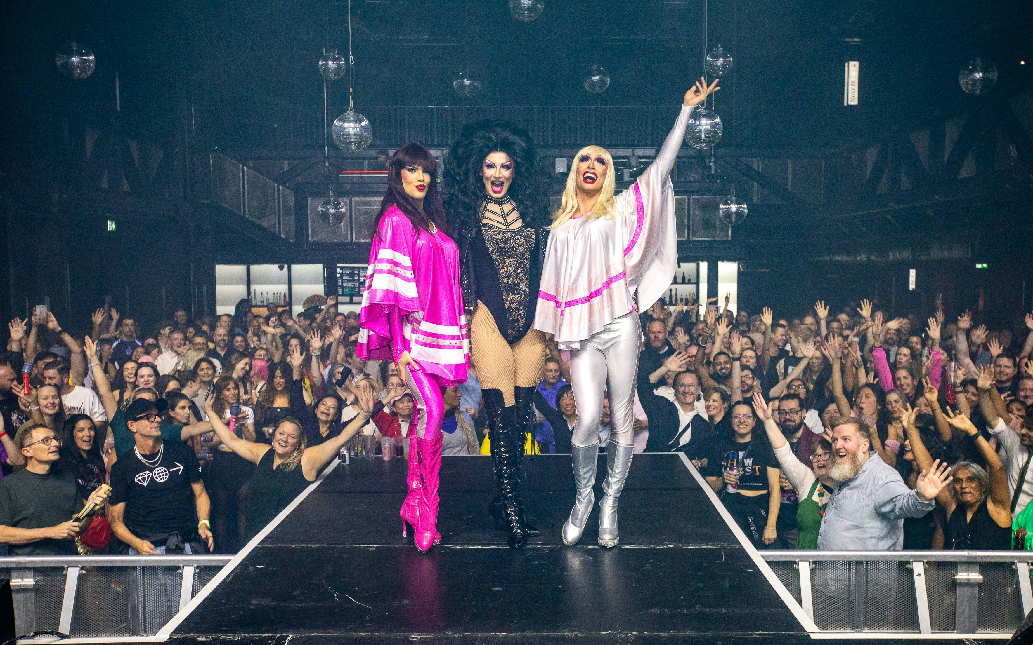 Drag performers on stage with cheering crowd at West End show.
