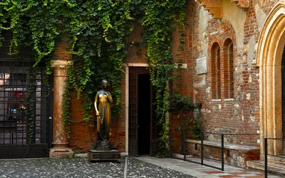 Juliet's bronze statue in Verona courtyard, Italy, surrounded by ivy-covered brick walls.