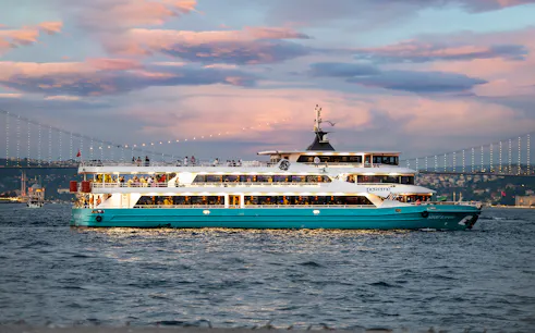 Bosphorus Dinner Cruise ship sailing at sunset with Istanbul skyline in the background.