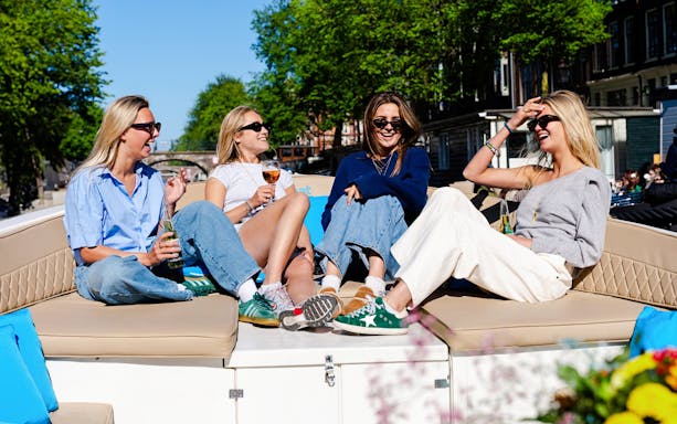Friends enjoying drinks on an open boat canal cruise in Amsterdam.