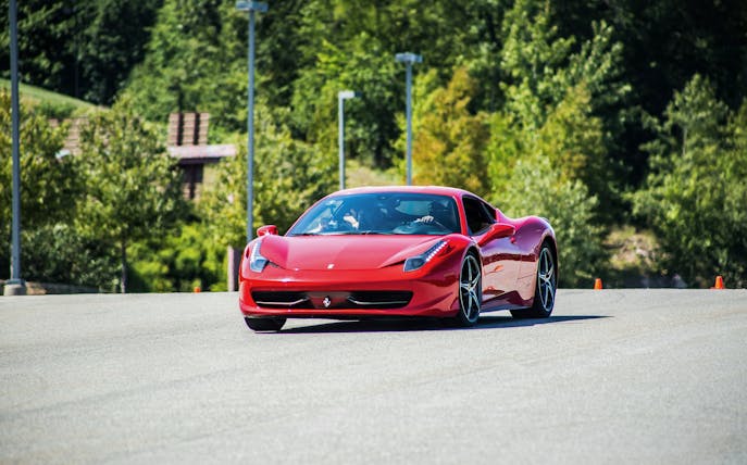 Red Ferrari 458 driving on a track surrounded by greenery.