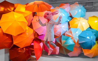 Person in rabbit costume with umbrella at Twist Museum, London, surrounded by colorful umbrellas.