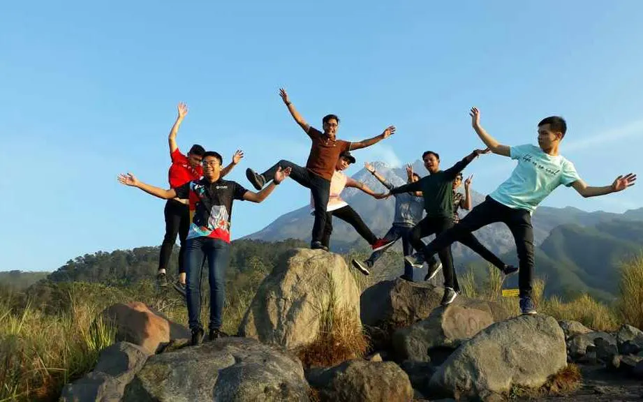 Group enjoying sunrise on Merapi Lava Tour, standing on rocks with mountain backdrop.