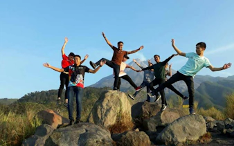 Group enjoying sunrise on Merapi Lava Tour, standing on rocks with mountain backdrop.