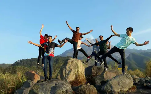 Group enjoying sunrise on Merapi Lava Tour, standing on rocks with mountain backdrop.