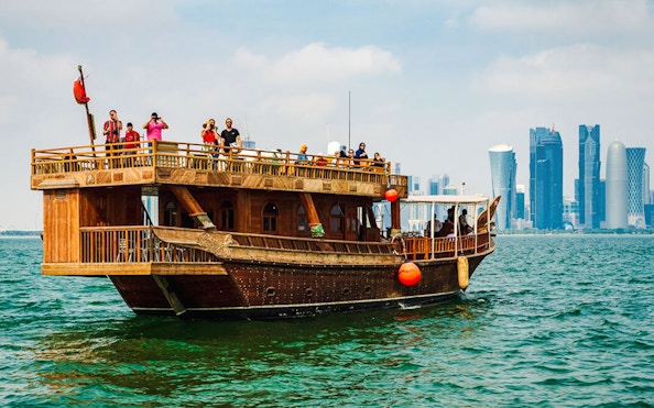 Dhow boat sailing with Doha city skyline in the background.