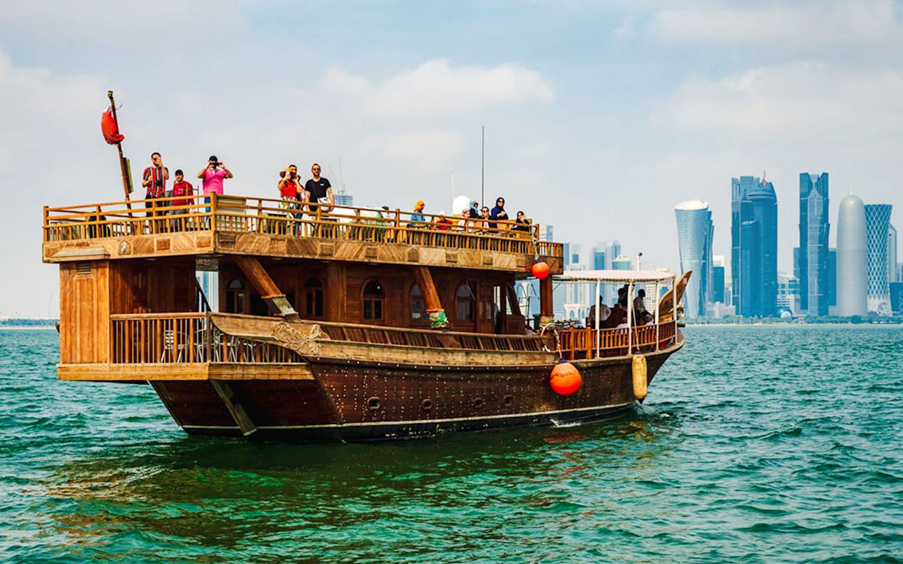 Dhow boat sailing with Doha city skyline in the background.
