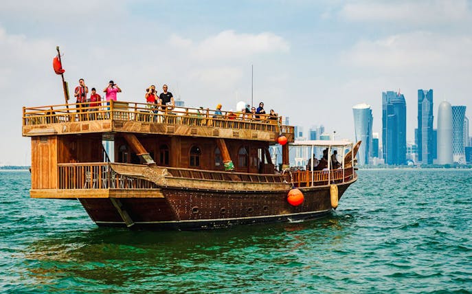 Dhow boat sailing with Doha city skyline in the background.