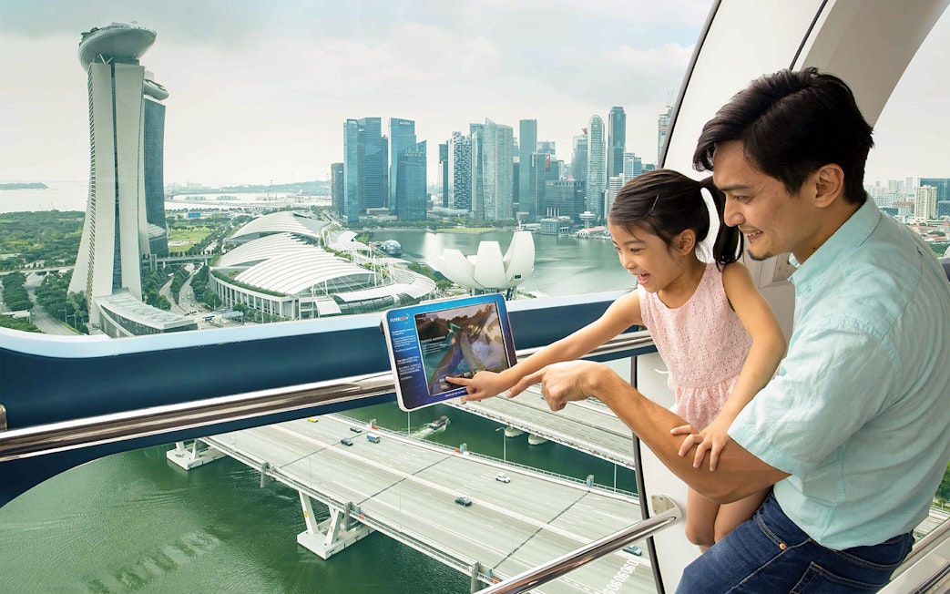 Father and daughter enjoying view from Singapore Flyer with Marina Bay Sands in background.