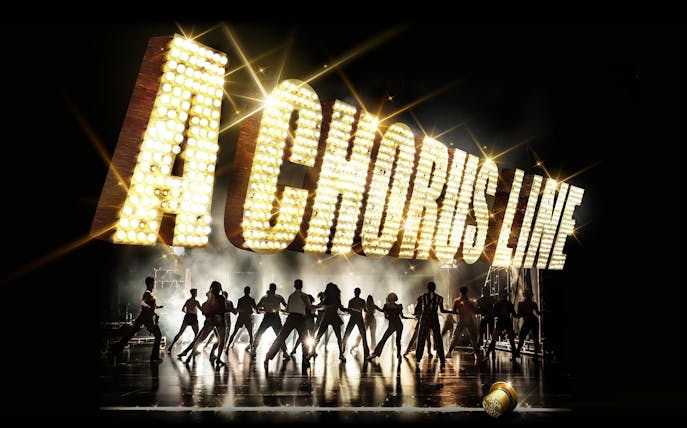 Dancers performing under illuminated "A Chorus Line" sign on stage.