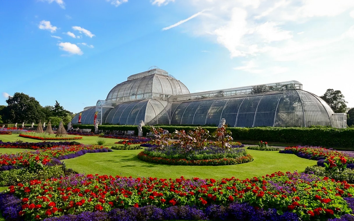 Kew Gardens Palm House with vibrant flower beds in London.