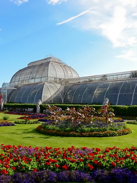 Kew Gardens Palm House with vibrant flower beds in London.