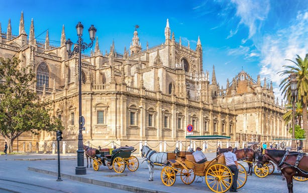 Seville Cathedral with horse-drawn carriages in front, showcasing Gothic architecture.