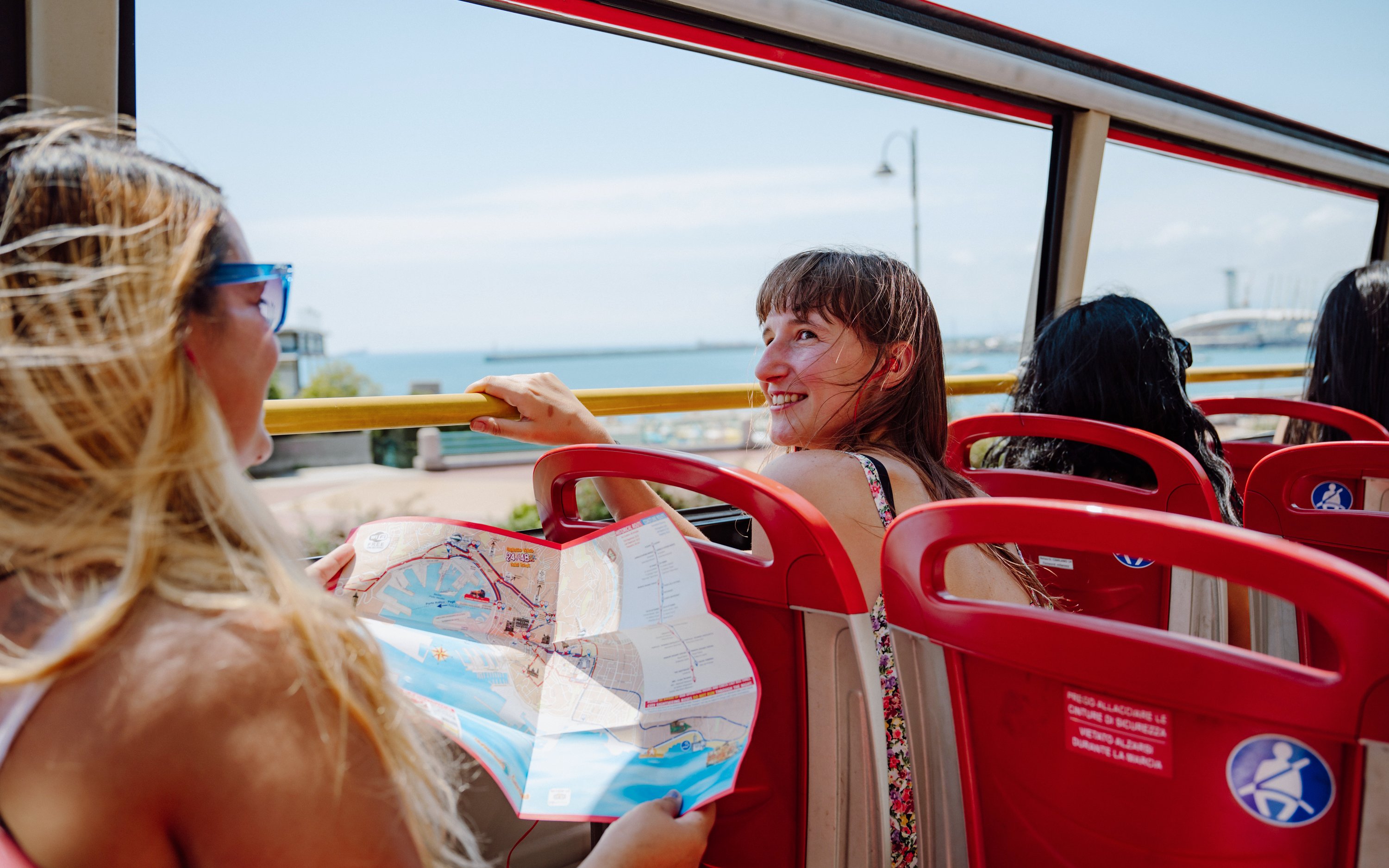 Passengers enjoying the City Sightseeing bus tour in Genova, Italy with a map.