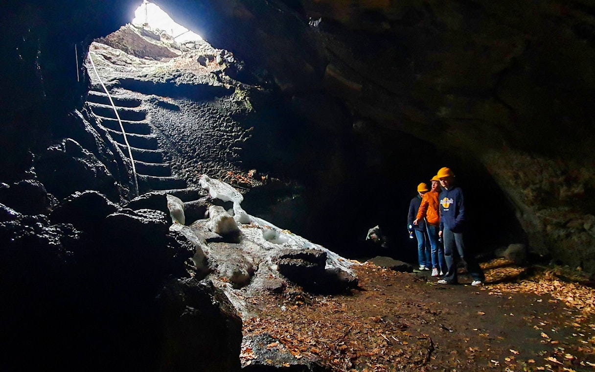 Visitors exploring a cave on Mount Etna with helmets and flashlights.