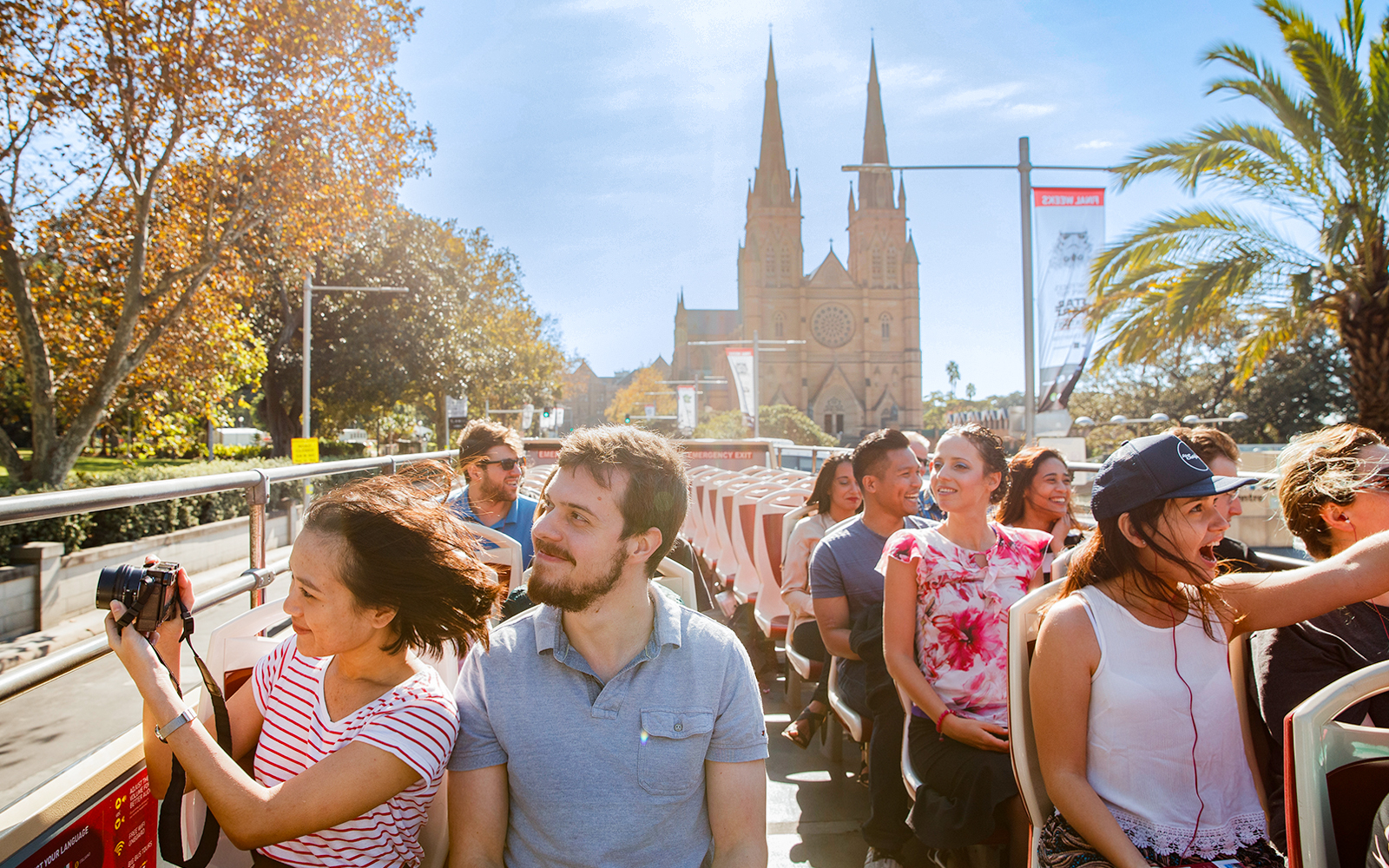 Open-top bus tour with people enjoying views of St. Mary's Cathedral, Sydney.