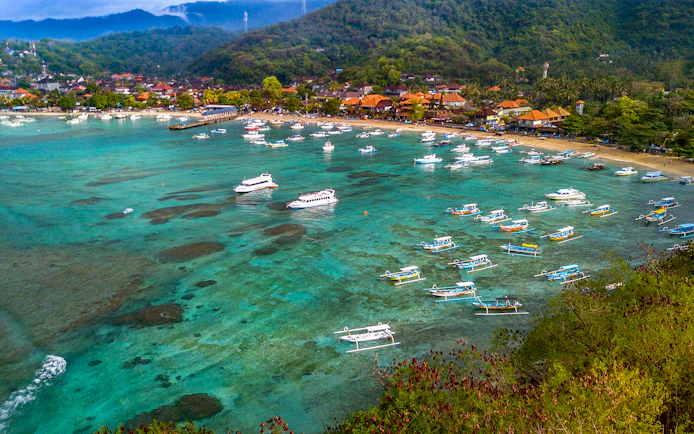 Boats anchored in Padang Bay, Bali, with lush hills and coastal village in the background.