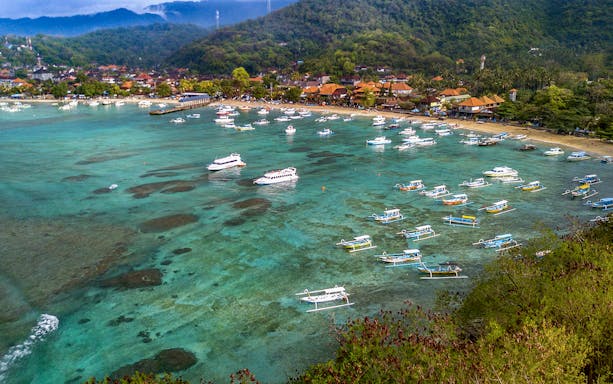 Boats anchored in Padang Bay, Bali, with lush hills and coastal village in the background.