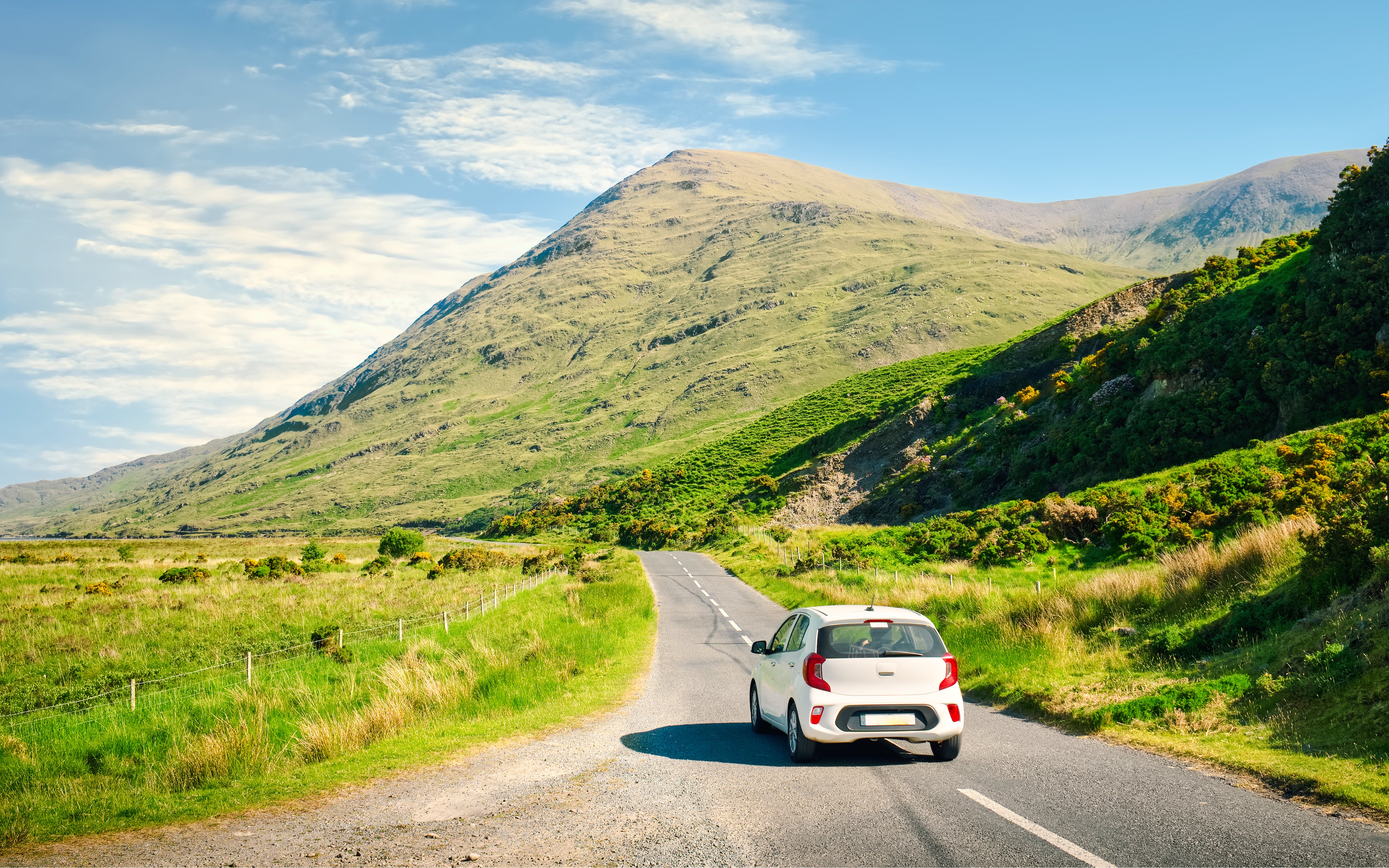 Car driving on a scenic road through lush green hills in Ireland.