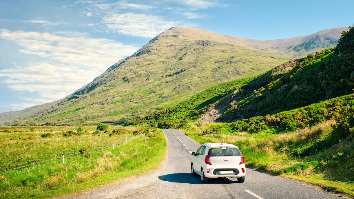 Car driving on a scenic road through lush green hills in Ireland.