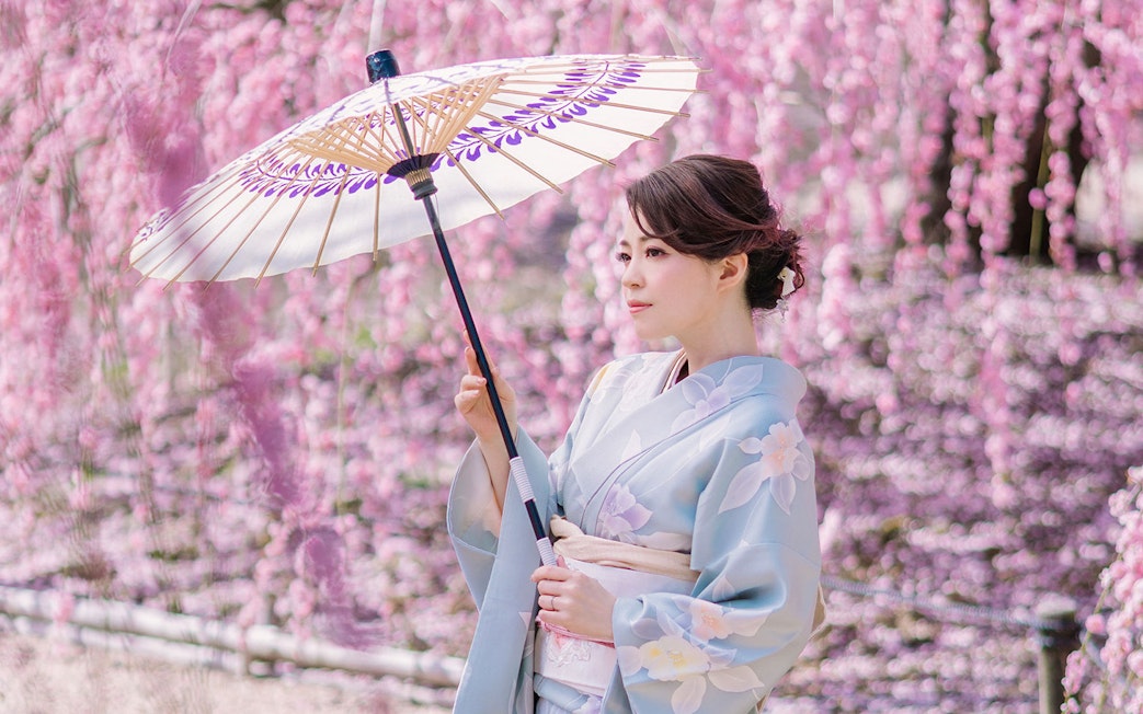 Woman in kimono with parasol in Kyoto Arashiyama during cherry blossom season.