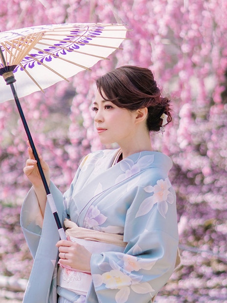 Woman in kimono with parasol in Kyoto Arashiyama during cherry blossom season.