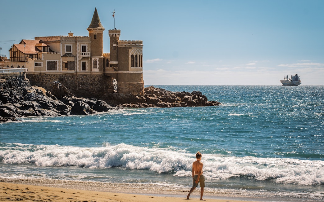 Wulff Castle on the rocky coast of Vina del Mar, Chile, with a ship in the distance.