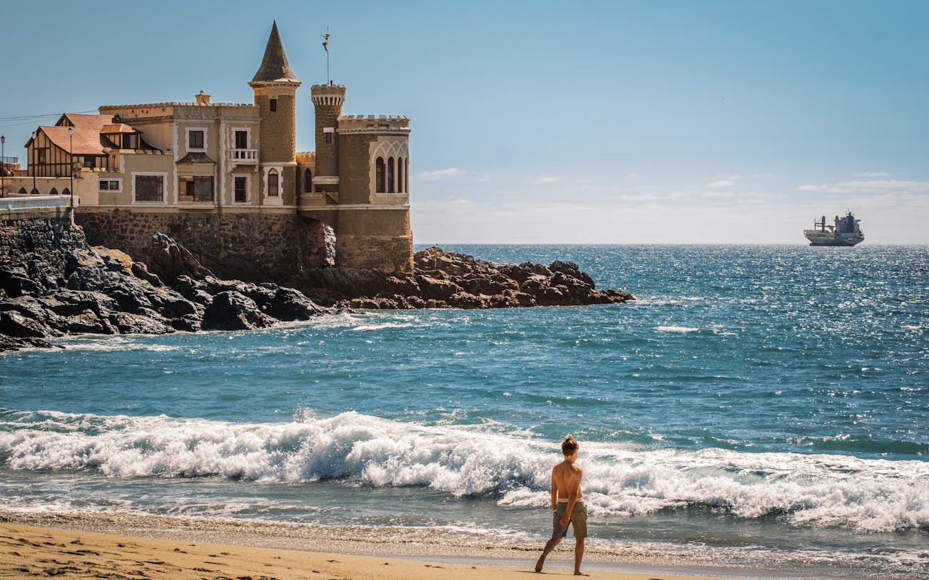 Wulff Castle on the rocky coast of Vina del Mar, Chile, with a ship in the distance.