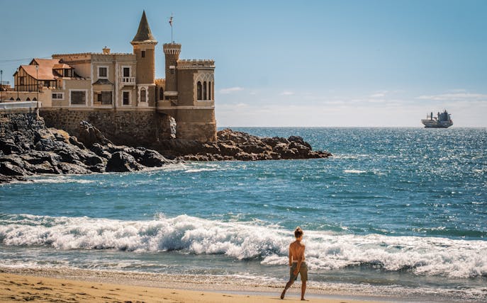 Wulff Castle on the rocky coast of Vina del Mar, Chile, with a ship in the distance.