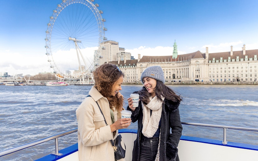 Two people enjoying a River Thames cruise with the London Eye in the background.