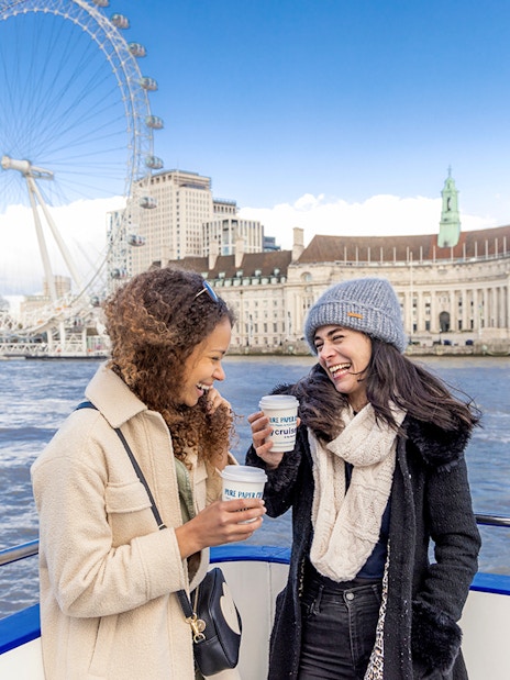 Two people enjoying a River Thames cruise with the London Eye in the background.