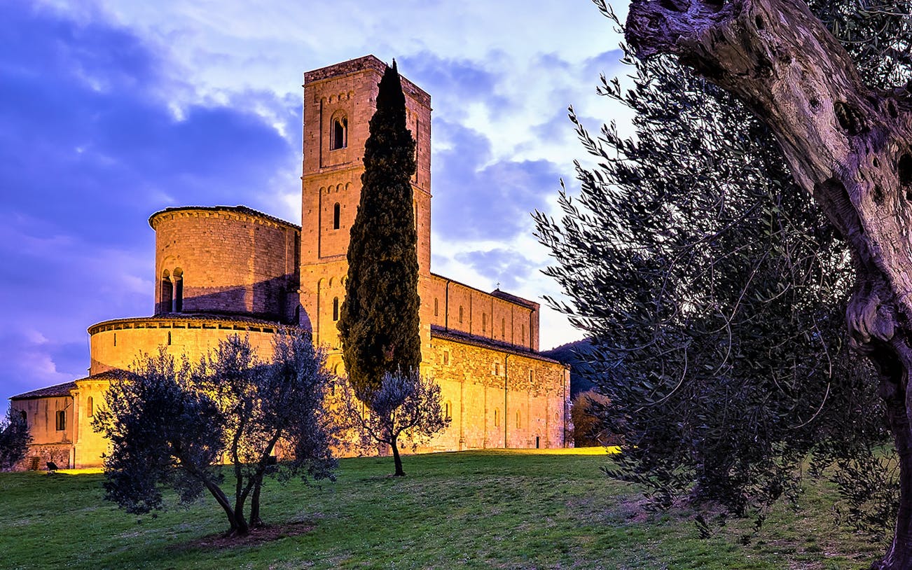 Abbey of Sant'Antimo at sunset near Montalcino, surrounded by olive trees.