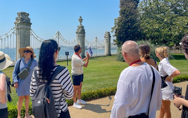 Tour group with guide at Dolmabahce Palace garden, Istanbul, near ornate gate and Bosphorus view.