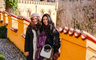 Tourists smiling at Hohenschwangau Castle, Germany, with yellow castle walls in the background.