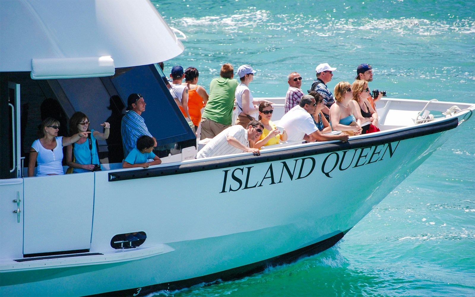 Tourists on "Island Queen" ferry cruising Biscayne Bay, Miami, with city skyline in the background.